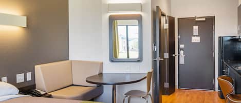 Habitación de hotel compacta con cama, una mesita, una silla, un escritorio y kitchenette.