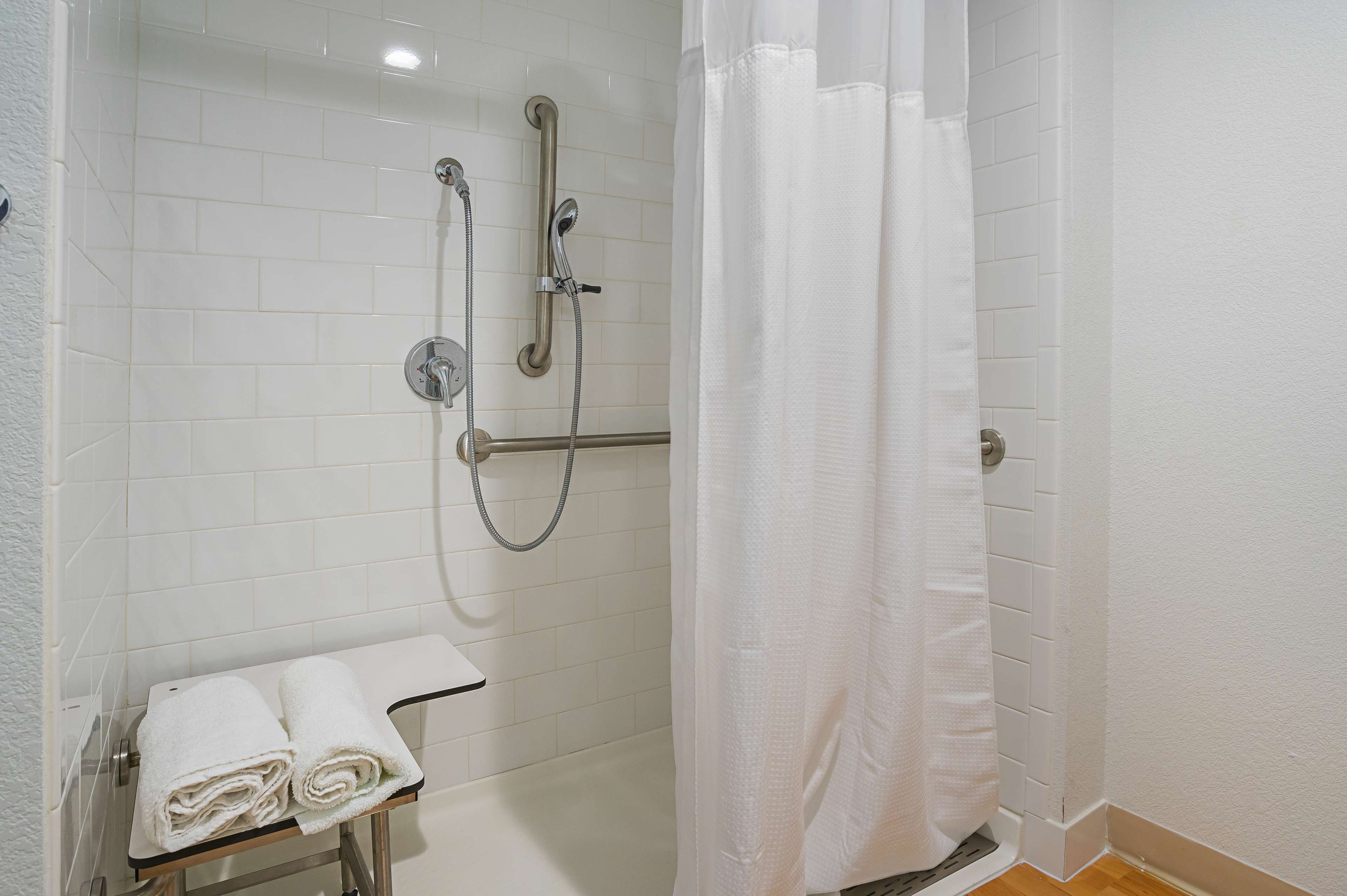 A shower area with white tiles, a glass door, and a towel rack with folded towels.