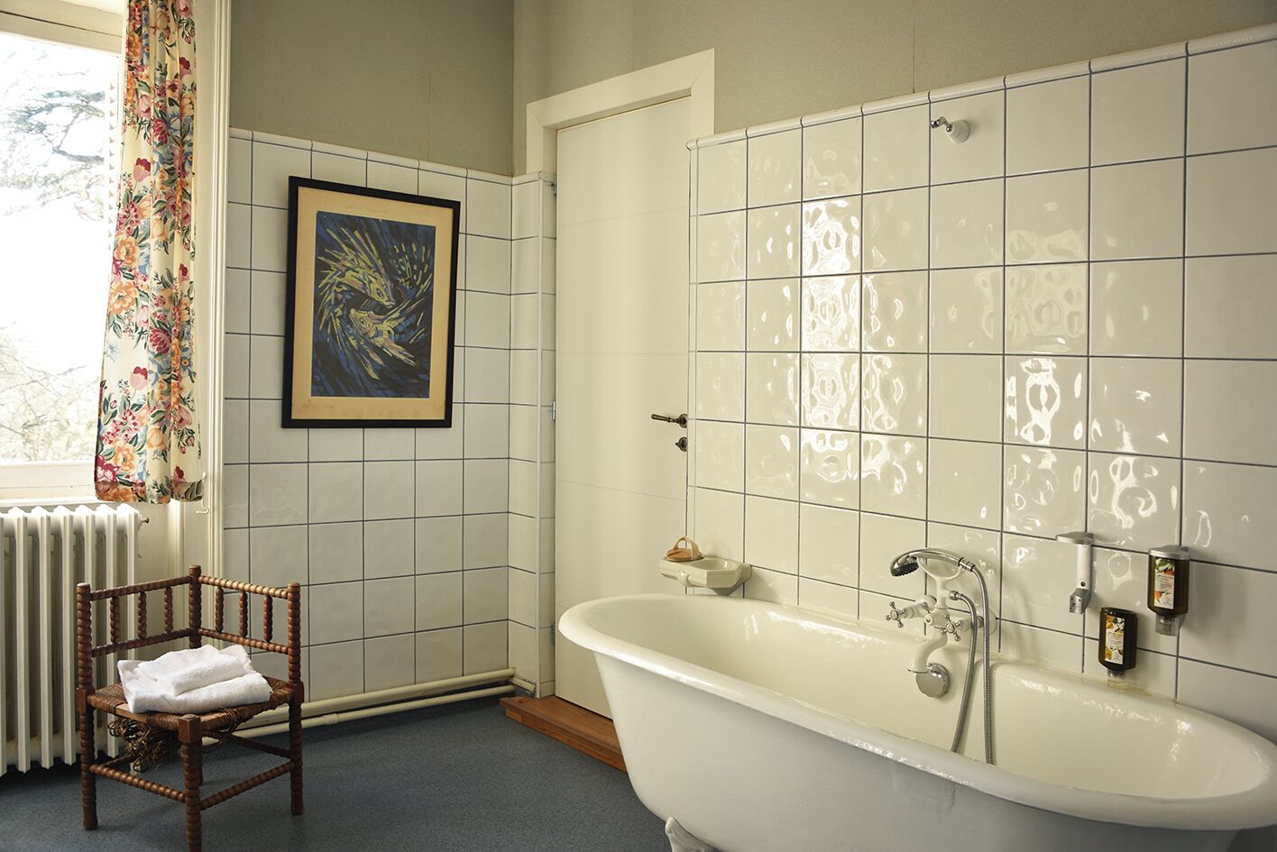Une salle de bain avec une baignoire, une œuvre d’art encadrée au mur et une chaise avec une serviette.
