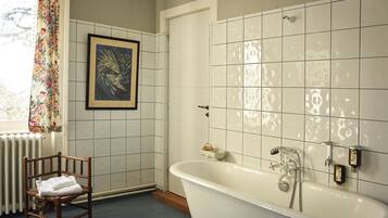 Une salle de bain avec une baignoire, une œuvre d’art encadrée au mur et une chaise avec une serviette.