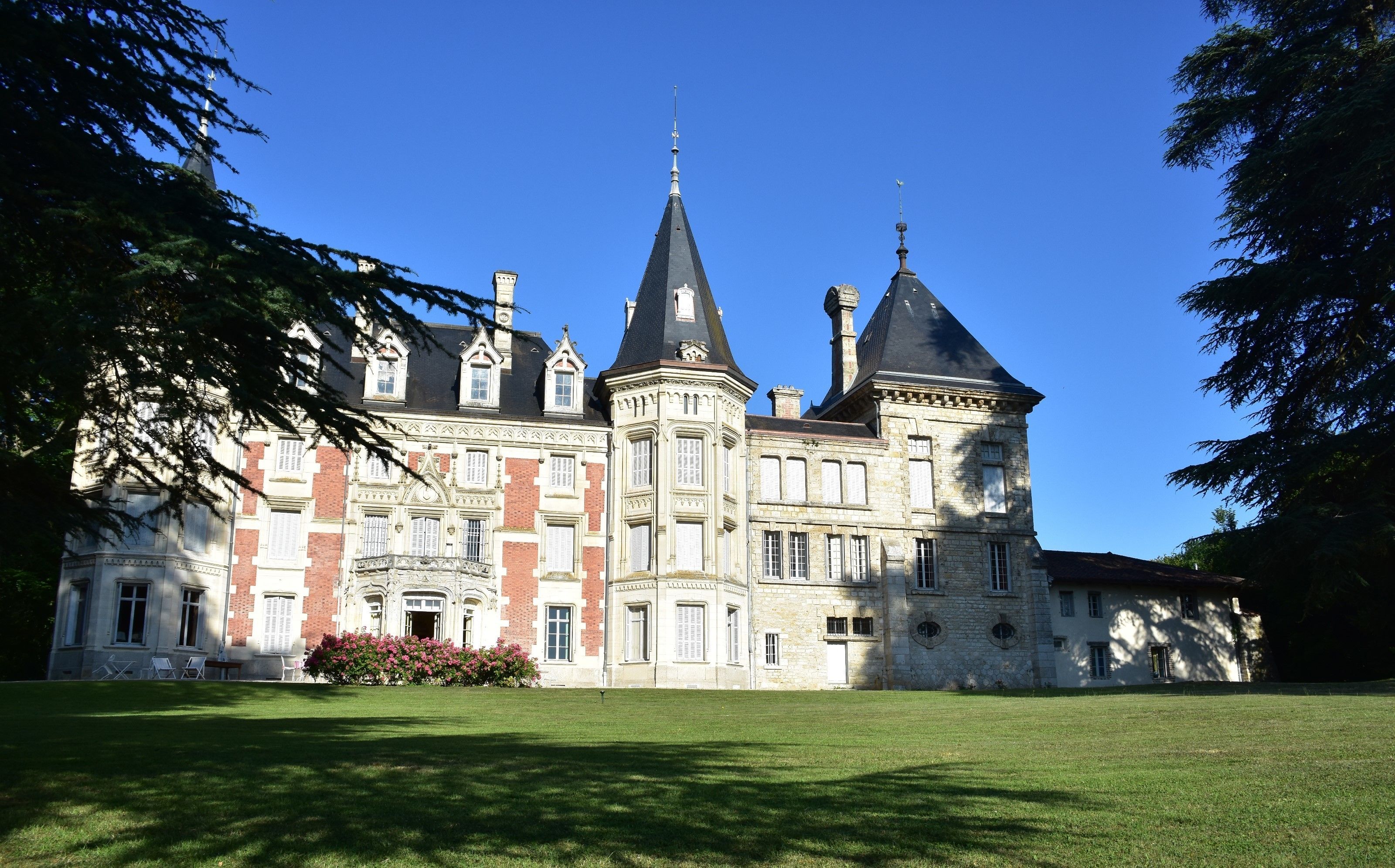 A large, historic building with multiple towers and a well-maintained lawn in front.
