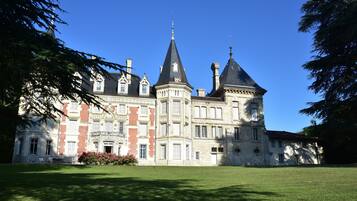 A large, historic building with multiple towers and a well-maintained lawn in front.