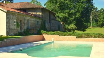 A pool area with a stone building and a grassy landscape.