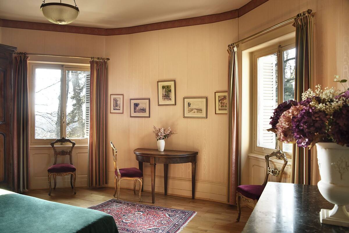 Ein Zimmer mit Holzwandverkleidung, einem runden Tisch mit Blumenvase, zwei Stühlen und gerahmten Bildern an der Wand.