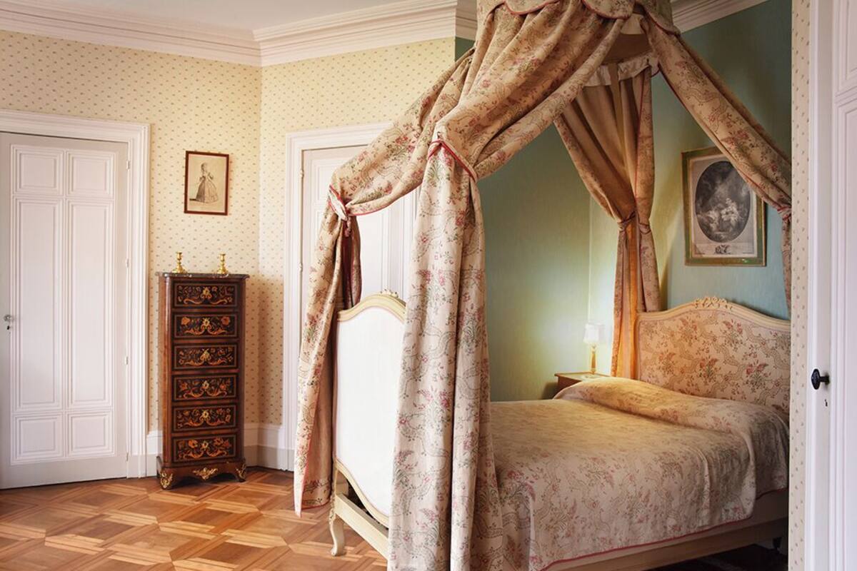 Ein Schlafzimmer mit einem Himmelbett, einem Holzkleiderschrank und einem gerahmten Bild an der Wand.