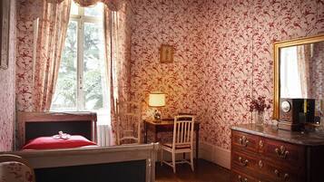 Una habitación con una cama, un tocador de madera, una silla, una mesa y una ventana con cortinas.
