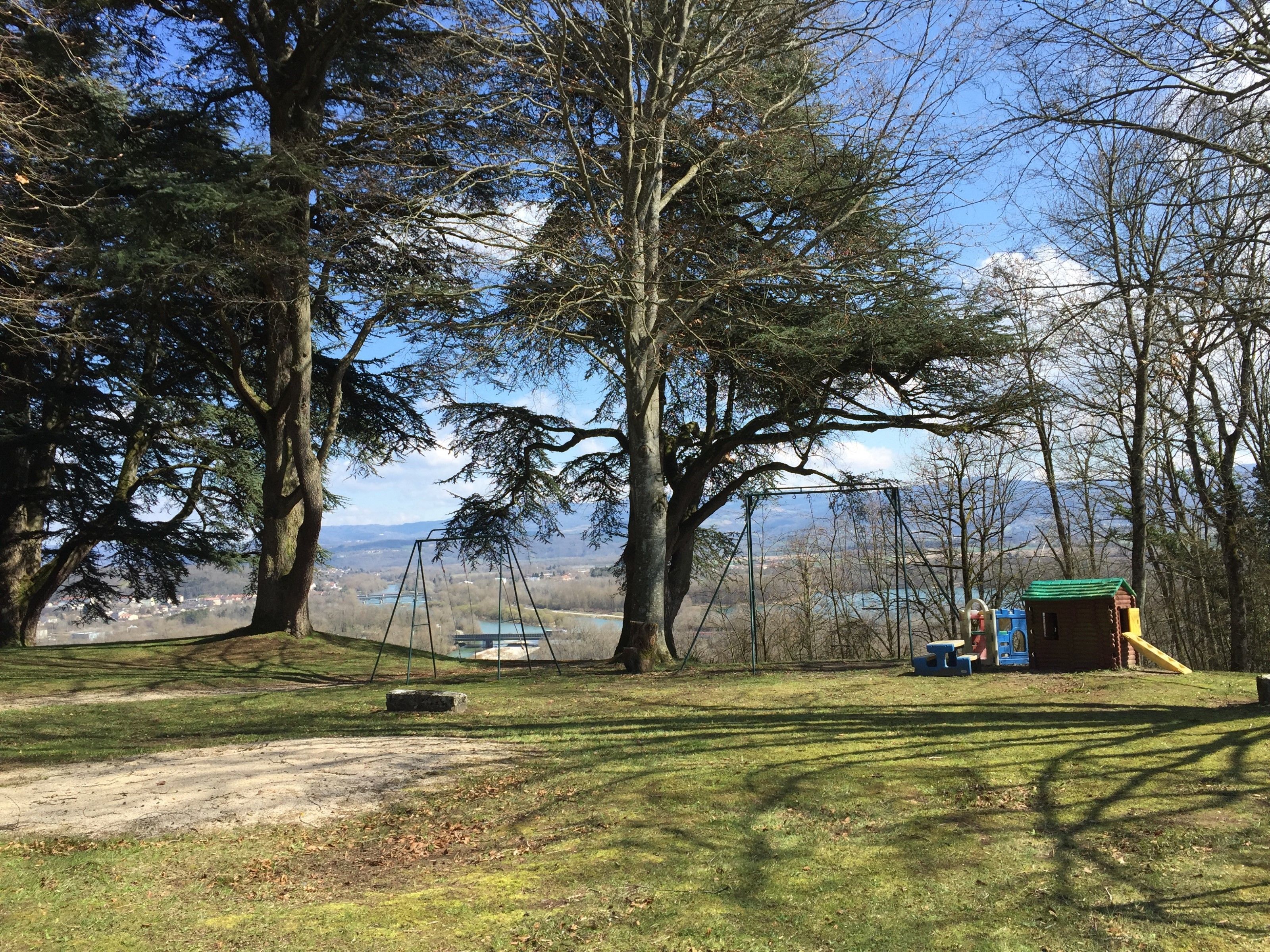 A park with swings, a small playhouse, and a dirt path.