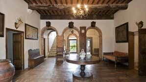 A spacious room with a large round table, wooden benches, and a chandelier.