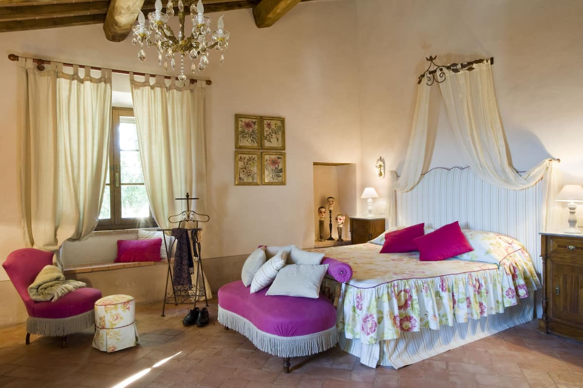 A bedroom with a bed, a chair, a small table, and a window with curtains.