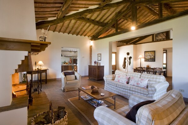 A cozy living room with a fireplace, a sofa, a coffee table, and a dining area with a table and chairs. - Azienda Agricola Montestigliano (Sovicille)