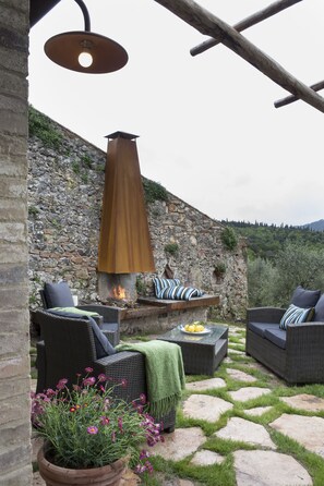 An outdoor seating area with wicker furniture, a stone wall, and a fire feature. - Azienda Agricola Montestigliano (Sovicille)