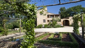 A stone building with a courtyard, a small pond, and a pergola with white flowers.