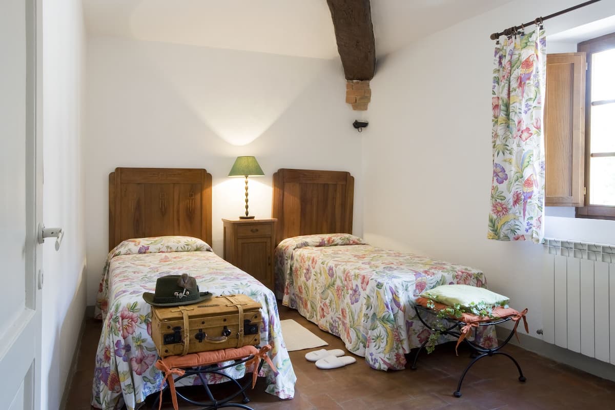 A bedroom with two beds, a nightstand with a lamp, a suitcase, and a radiator.