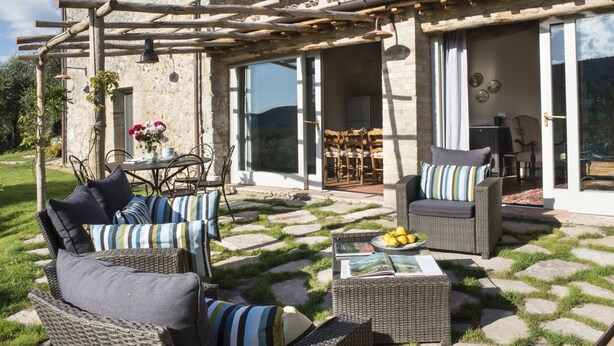 A patio area with wicker furniture, a table with a plate of lemons, and a pergola with hanging lights.