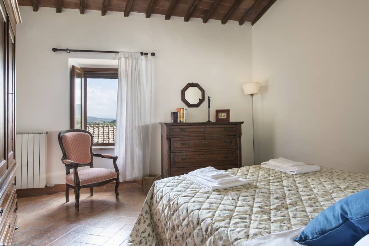 A bedroom with a bed, a chair, a dresser, a mirror, and a window with curtains.