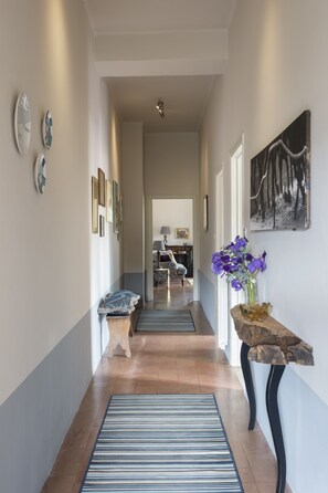 A hallway with a striped rug, a wooden bench, a vase with flowers, and framed pictures on the walls. - Azienda Agricola Montestigliano (Sovicille)