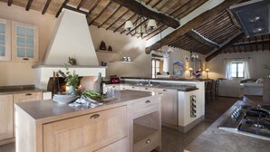 A spacious kitchen with wooden beams, a large island with drawers, a gas stove, and a window providing natural light.