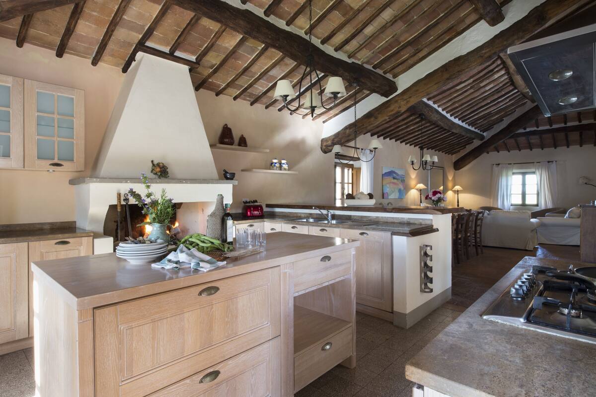 A spacious kitchen with wooden beams, a large island with drawers, a gas stove, and a window providing natural light.