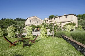 A rustic villa with a garden, two wooden chairs, and a stone wall. - Azienda Agricola Montestigliano (Sovicille)