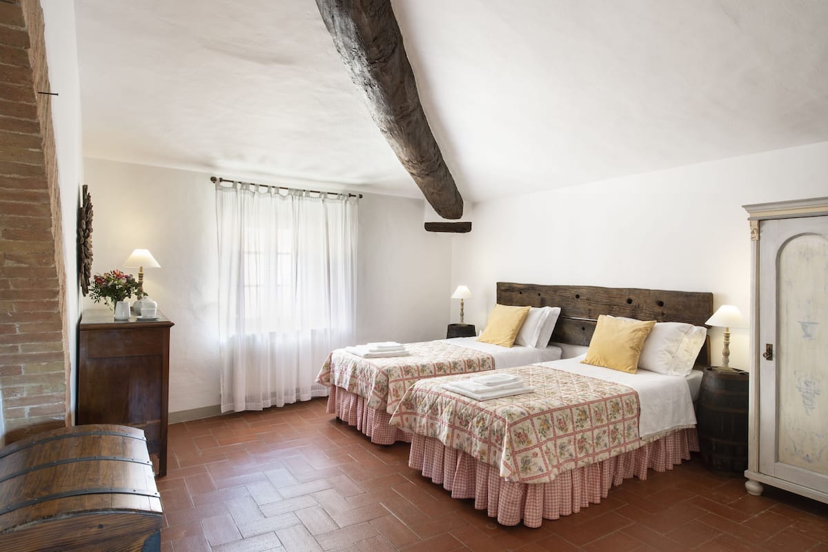 A bedroom with two beds, a wooden headboard, a wooden cabinet, and a bench.