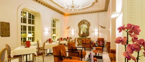 Vestíbulo de hotel con candelabro, espejo decorativo y zonas de estar confortables.