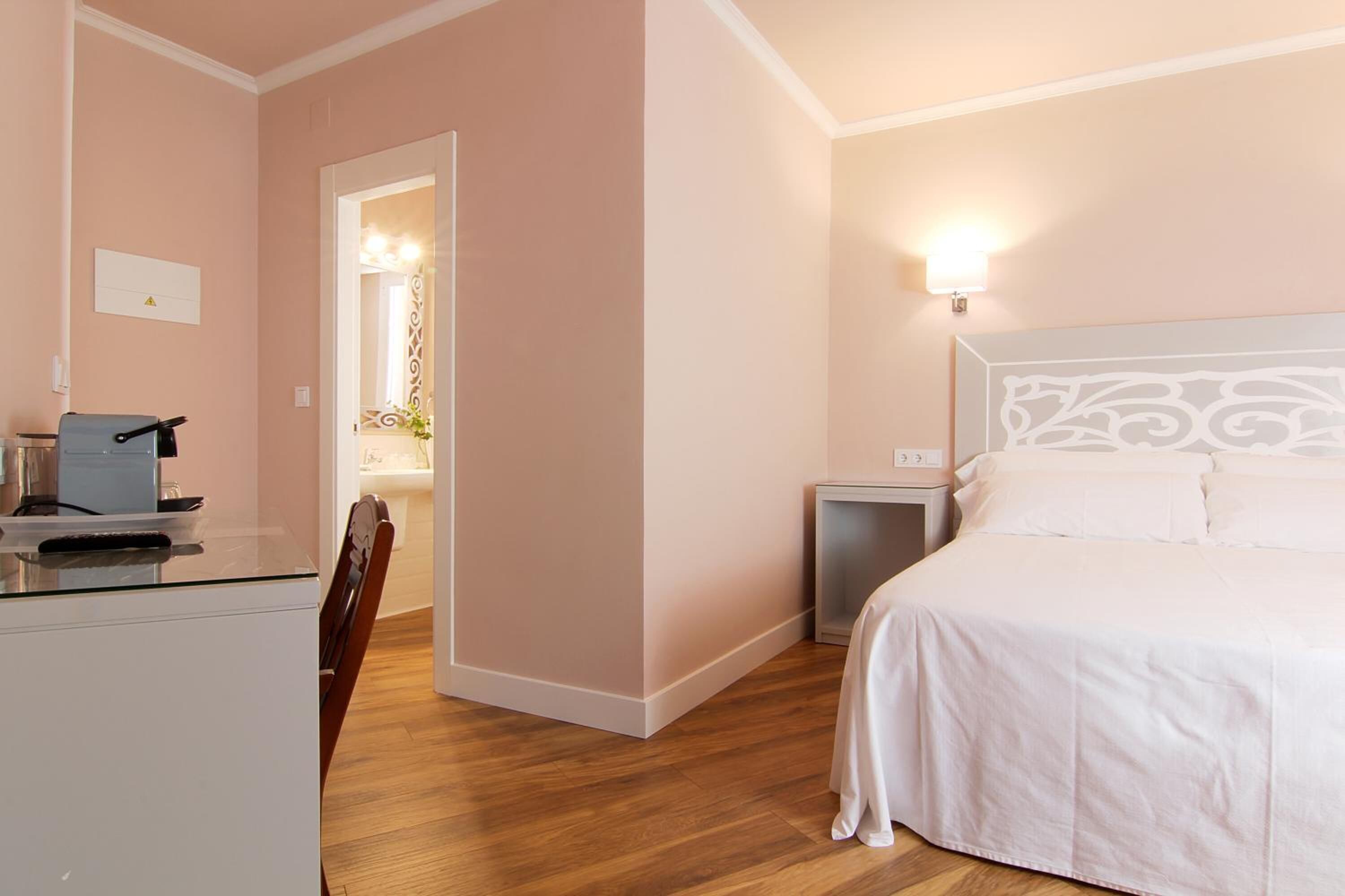 Una camera d'albergo con un letto, un comodino e una scrivania con una sedia.
