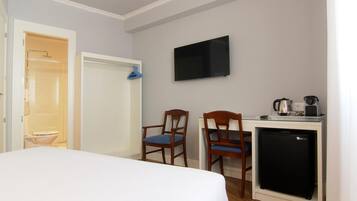 Una habitación de hotel con cama, escritorio con computadora, televisor y kitchenette.