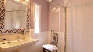 A bathroom with a white sink, a mirror with decorative frame, a shower with glass doors, and a wooden chair. - Hostal los Castañuelos (Candeleda)