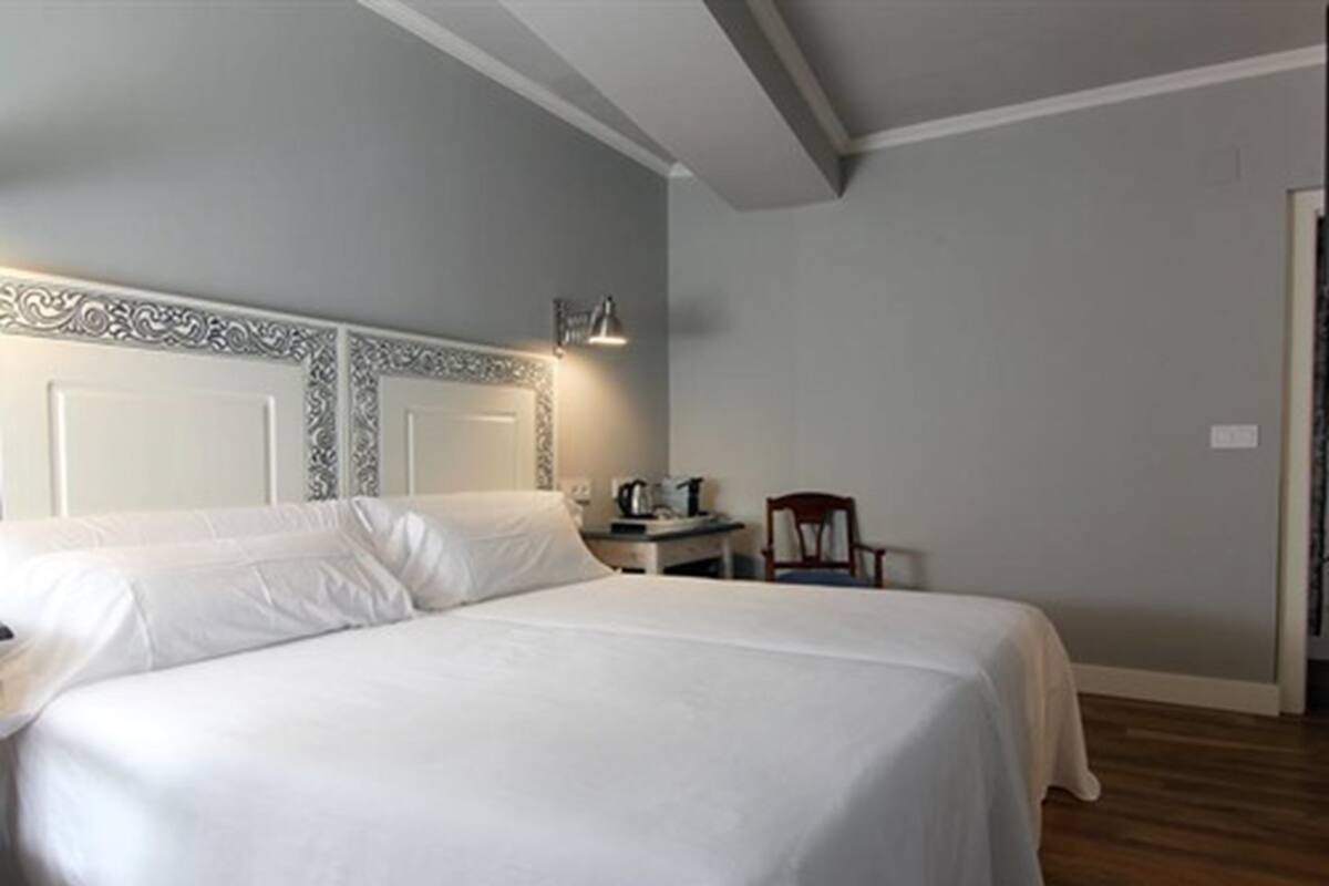 Ein Hotelzimmer mit einem großen Bett, einem Nachttisch, einem Sessel und einem Schreibtisch mit Lampe.
