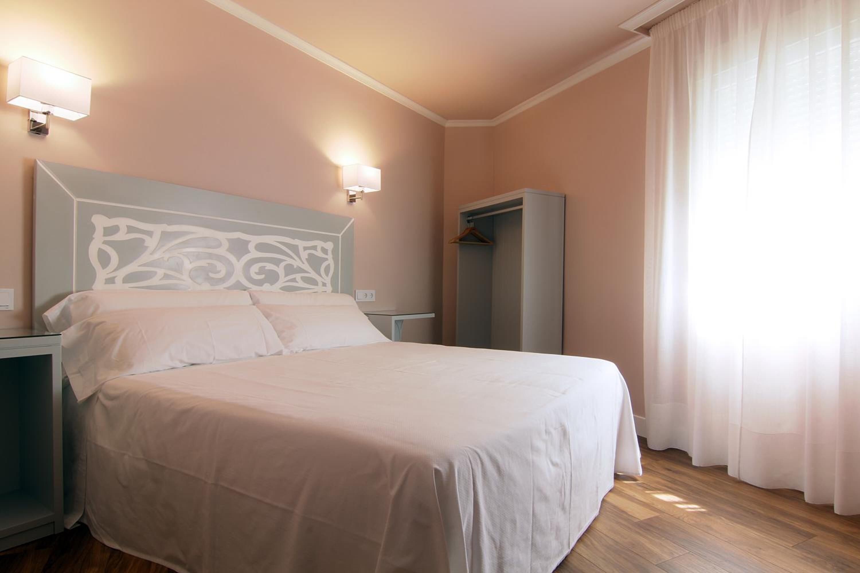 A neatly made bed in a room with a headboard, bedside lamps, and a wardrobe.