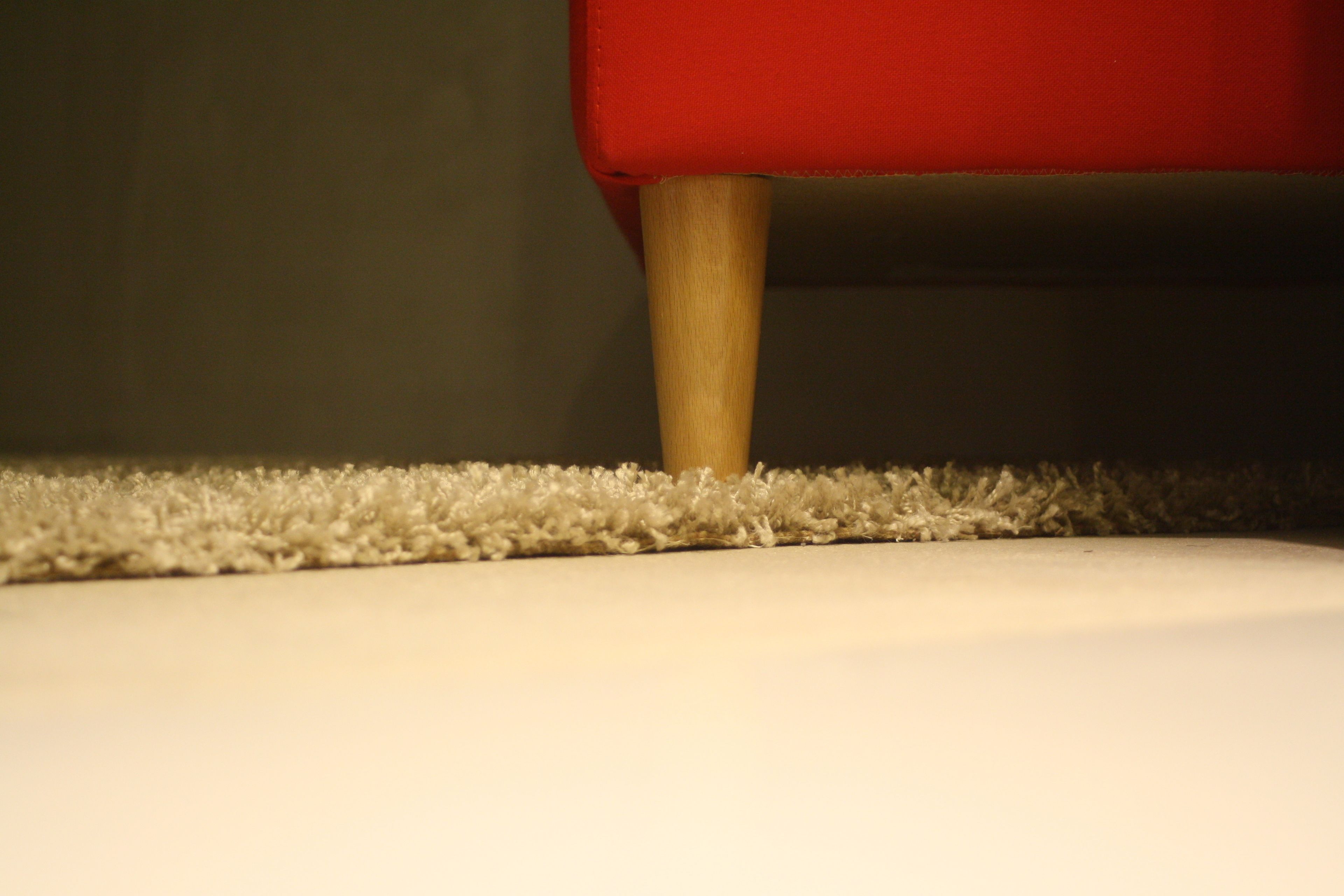 Detalhe de uma perna de cadeira vermelha sobre um piso coberto de carpete.