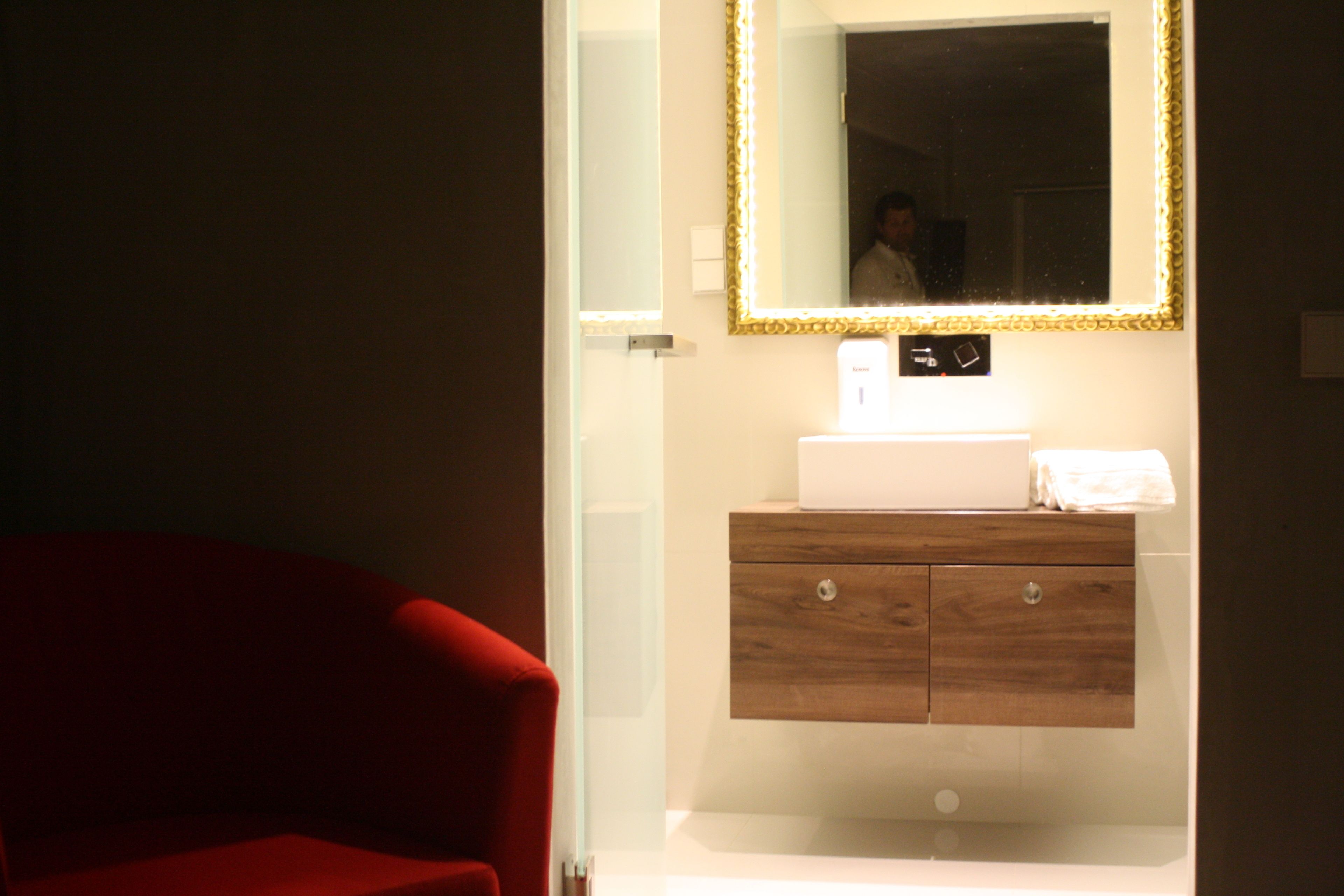 Un baño con tocador de madera, lavabo blanco y espejo con marco dorado.