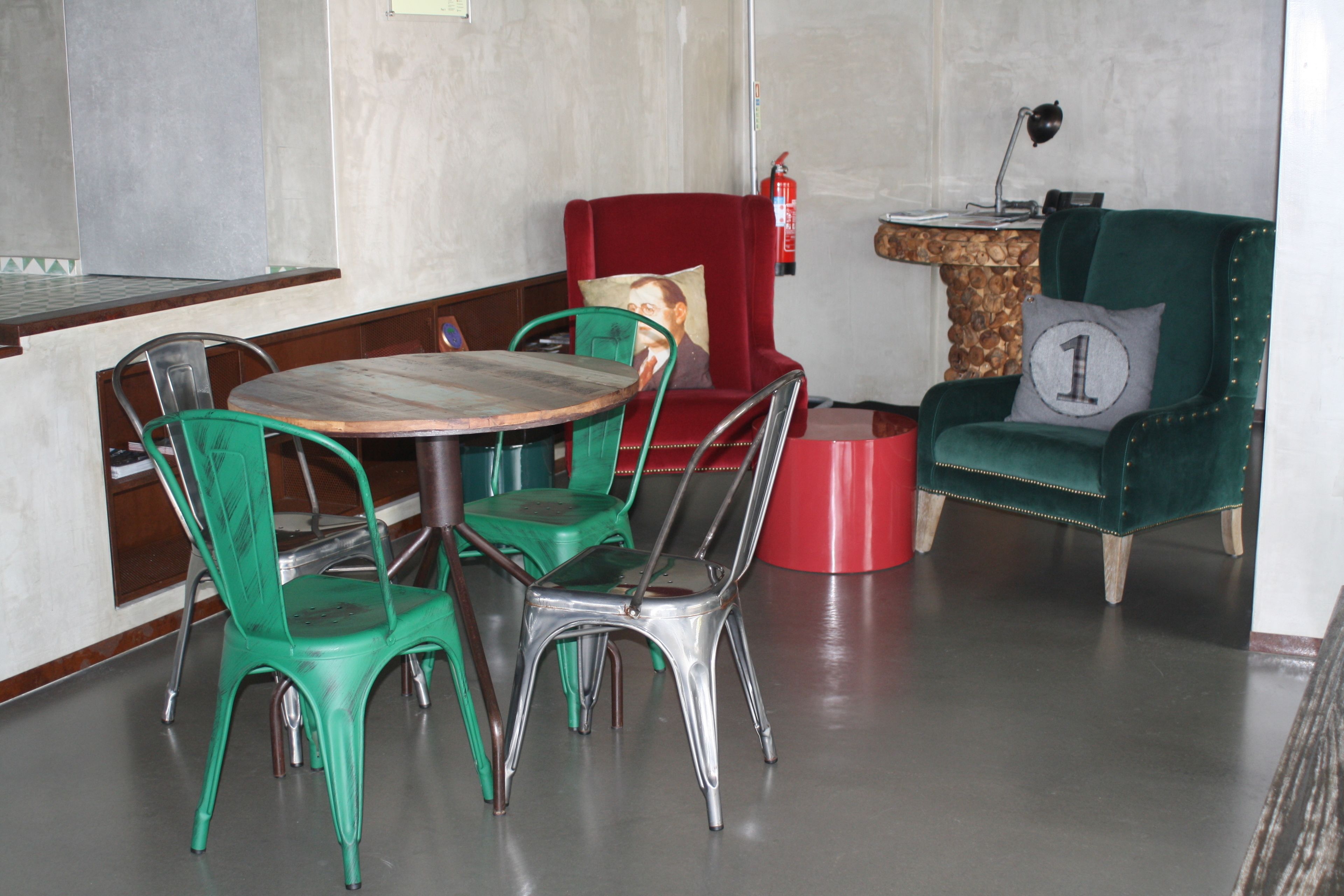 Un comedor con una mesa redonda, sillas verdes, una silla roja con cojín y una butaca verde de terciopelo con cojín.