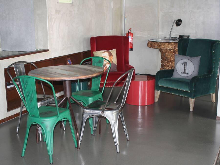 Un comedor con una mesa redonda, sillas verdes, una silla roja con cojín y una butaca verde de terciopelo con cojín.