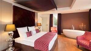 Een moderne hotelkamer met een groot bed, een zithoek met een fauteuil, een ligbad en een raam met gordijnen.