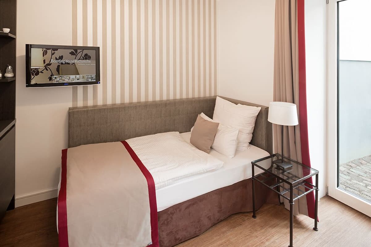 A neatly made bed with a red and white bedspread, a bedside table with a lamp, and a striped wall.