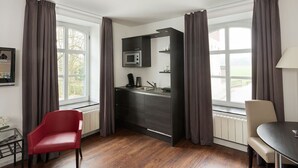 Een kleine kamer met een keukenhoek, een eettafel en een rode stoel.
