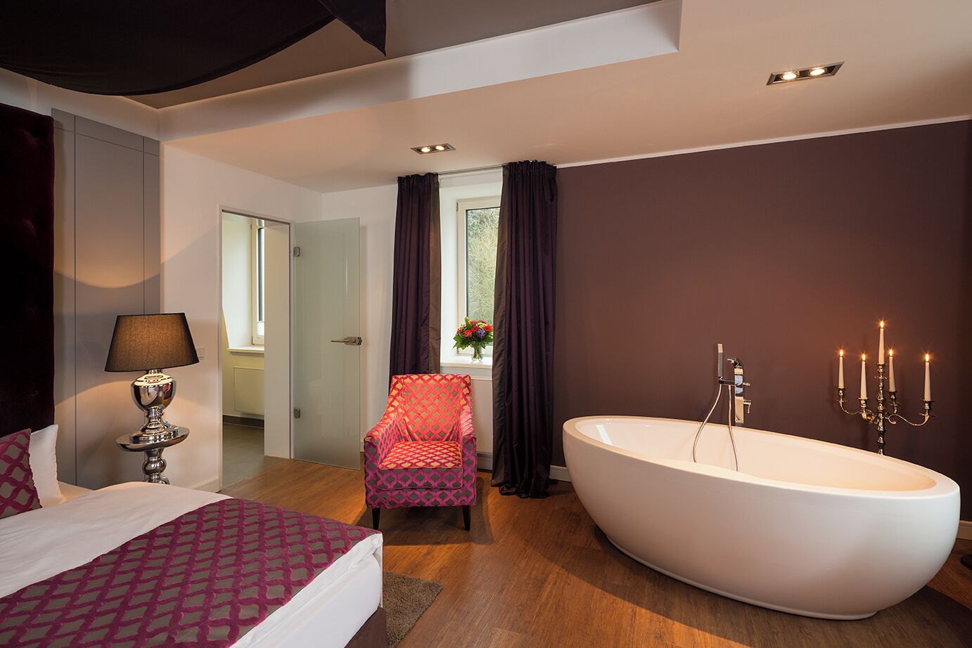 Quarto moderno com cama grande, área de estar, banheira e banheiro com candelabro.