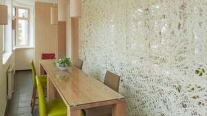 Een moderne eetruimte met een houten tafel, groene en bruine stoelen en een decoratieve witte muur.