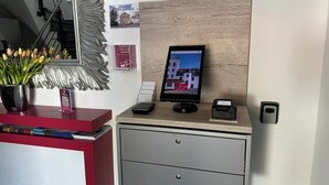 Een receptiebalie met een digitaal scherm, een QR-code, een kleine printer en een potplant.