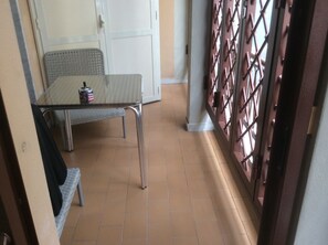 A small, enclosed balcony area with a metal table and a bench, a white door, and a metal gate with a grid pattern. - B&B Cuore di Salerno (Salerno)