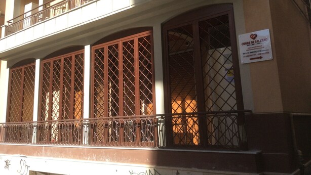 Un immeuble doté d’un balcon, de grandes fenêtres avec des grilles en métal et d’une enseigne sur le mur.