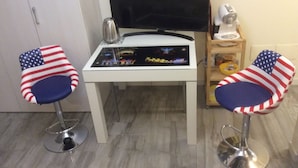 Une petite pièce avec un bureau blanc, un téléviseur à écran plat et deux chaises ornées de motifs représentant le drapeau américain.