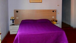 A bedroom with a wooden headboard, a purple bedspread, a nightstand with a vase of flowers, and a framed picture on the wall. - Bed and Breakfast La Torretta (Cascina)