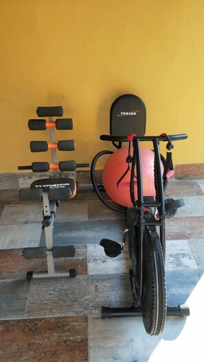 Ein stationäres Fahrrad und eine Bank mit Kurzhanteln vor einer gelben Wand.
