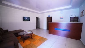A hotel lobby with a reception desk, a brown sofa, a coffee table, and a television screen.