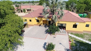 A yellow building with a red-tiled roof, a paved courtyard, and a palm tree.
