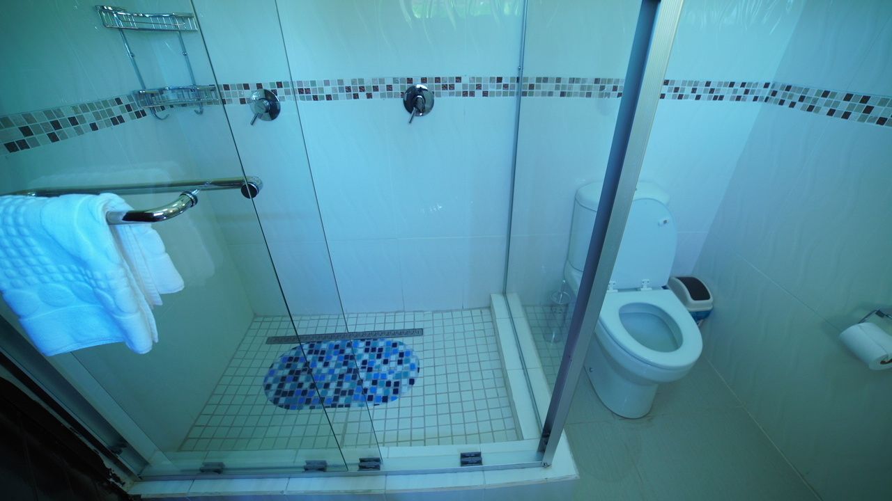 Un espace douche doté d’une porte en verre, d’un sol carrelé, de toilettes blanches et d’un porte-serviettes.