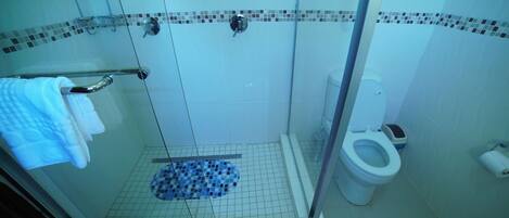 Un espace douche doté d’une porte en verre, d’un sol carrelé, de toilettes blanches et d’un porte-serviettes.