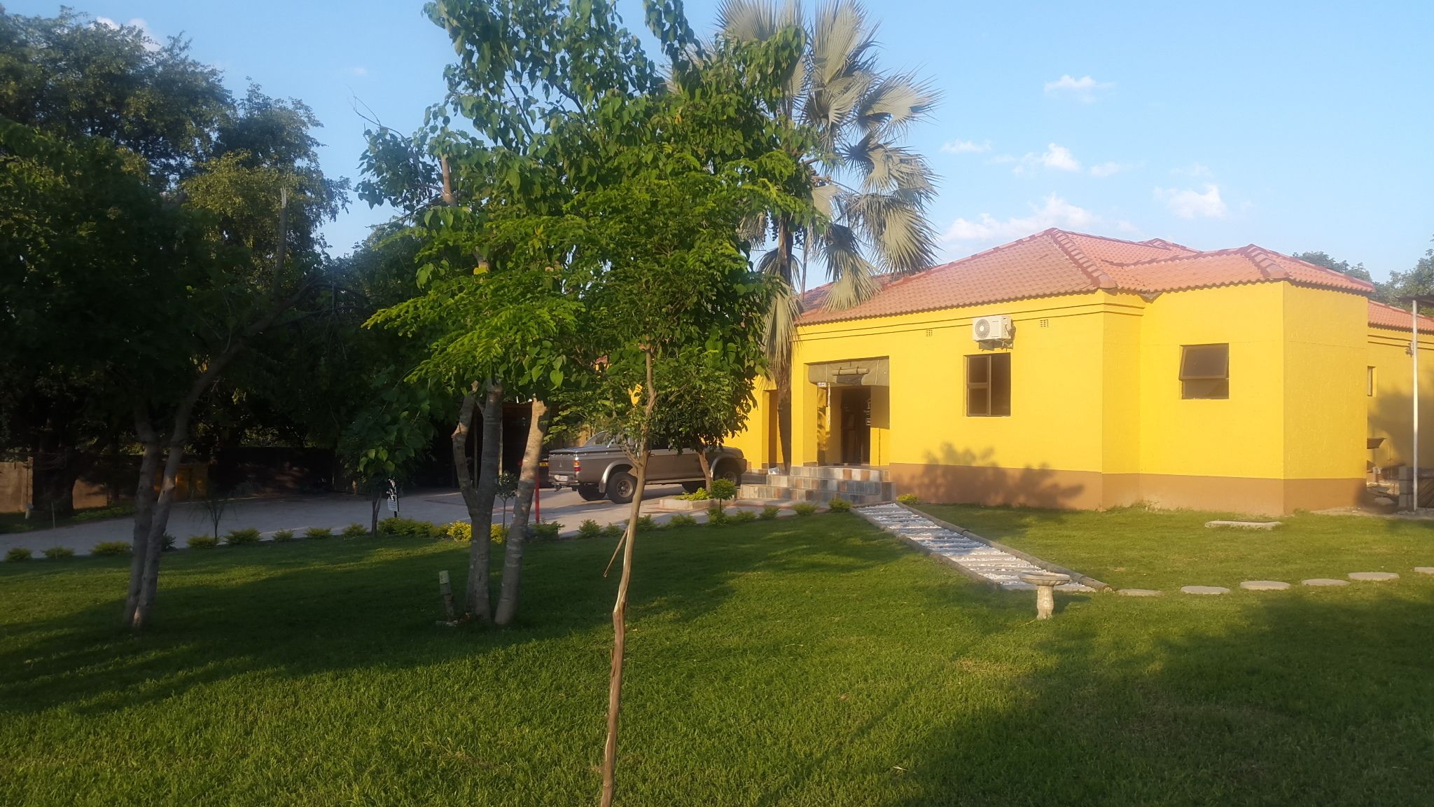 A yellow building with a red roof, surrounded by green grass and trees.